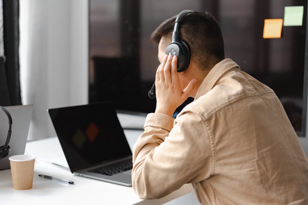 pexels photo 7681302 A man wearing headphones works at a laptop in a modern office setting.